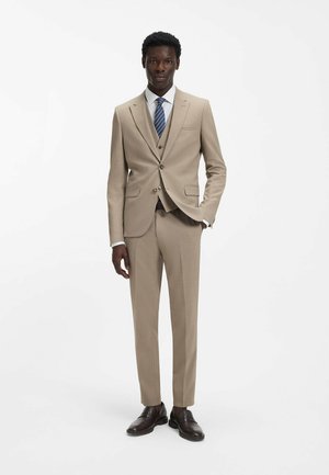 Beige tailored suit made of textured fabric, featuring two buttons, notch lapels, and a chest pocket. Worn with a white shirt and striped tie.