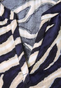 V-neck blouse featuring a tiger stripe pattern in beige and navy blue, with a smooth texture and contrasting stitching along the edges.