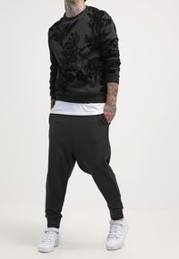 Svart sweatshirt med texturerat blommönster, ihop med svart, baggy joggers och vita sneakers. Enkelt, avslappnat klädesplagg.