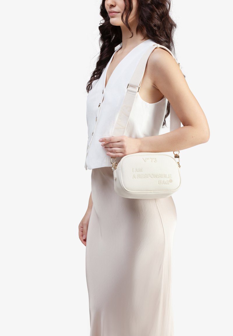 Bolso bandolera blanco hecho de material texturizado, con el texto embossado "SOY UN BOLSO RESPONSABLE" y una correa beige desmontable con acentos metálicos.