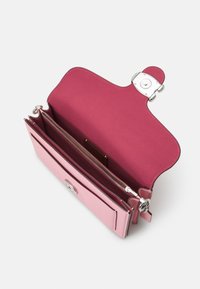 Sac à main en cuir rose avec une surface extérieure lisse. L'intérieur présente une doublure bordeaux foncé, une poche centrale zippée et des détails de ferrures à clip.