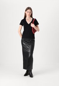Juodas trumpas rankovėmis V formos iškirpimas viršus, derinamas su juoda odine midi sijonu su priekinėmis plyšiais. Modelis laiko raudoną rankinę ir dėvi juodas kulkšnių batus.