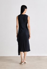 Sleeveless, dark navy, knee-length dress with a textured finish and an asymmetrical hem, complemented by a subtle back keyhole detail.