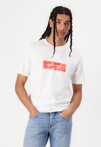 Hvid bomulds t-shirt med et rødt logo print i rektangulært design. Rund hals og kortærmet med en afslappet pasform.