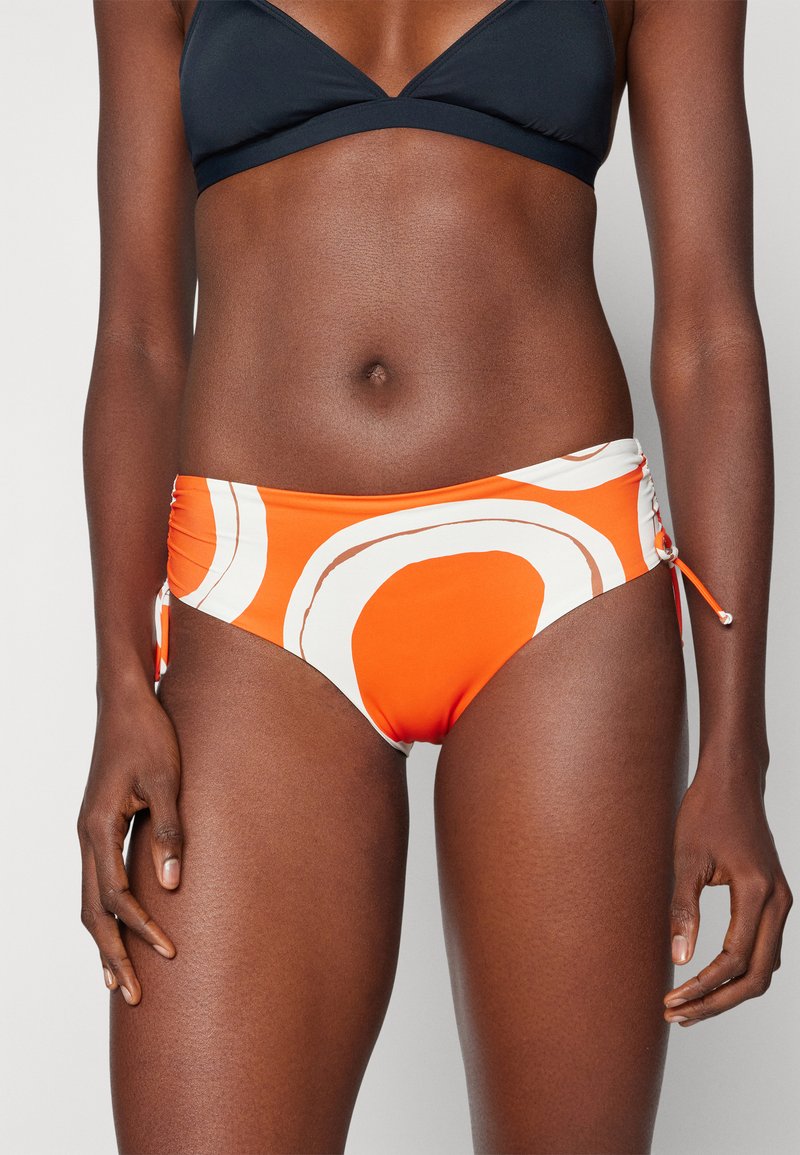 Narancssárga és fehér mintás bikini alsó, oldalsó megkötőkkel, sima textúrával és félmagas derék dizájnnal, amely kényelmes illeszkedést biztosít.