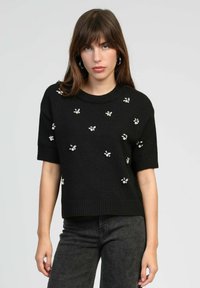 Pull noir à manches courtes avec ourlet côtelé, orné de motifs floraux en petites perles sur le devant.
