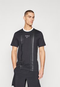 Zwarte T-shirt met korte mouwen en een witte ronde halslijn, gekenmerkt door verticale zwarte strepen en een "Fútbol" grafiek boven een Nike-logo.