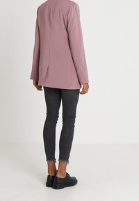 Jasnoróżowy blazer z tylnym rozcięciem, w połączeniu z ciemnoszarymi, postrzępionymi dżinsami skinny i czarnymi sznurowanymi butami. Gładka faktura, dopasowany krój.