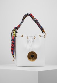 Vit fusk läder hinkväska med ett knutet, flerfärgat mönstrat handtag och hardware i guldton som har en rund logotags.