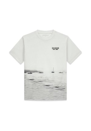 Hellgraues Baumwoll-T-Shirt mit einem fotografischen Druck von Booten auf dem Wasser. Enthält den Schriftzug "GUESS EST. 1981" in Schwarz auf der Brust. Kurze Ärmel.