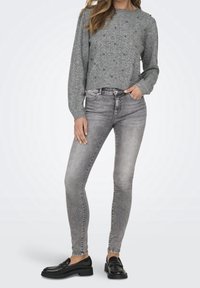 Pull en tricot gris avec motif texturé et petites décorations subtiles. Associé à un jean skinny gris clair et des mocassins noirs.