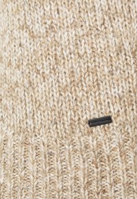 Tissu beige et blanc en tricot avec une texture côtelée et une petite étiquette rectangulaire noire portant la mention "Tom Tailor" attachée.