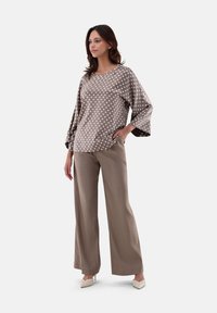 Blusa marrone a pois con maniche larghe abbinata a pantaloni beige a vita alta. La modella indossa décolleté color crema a punta.