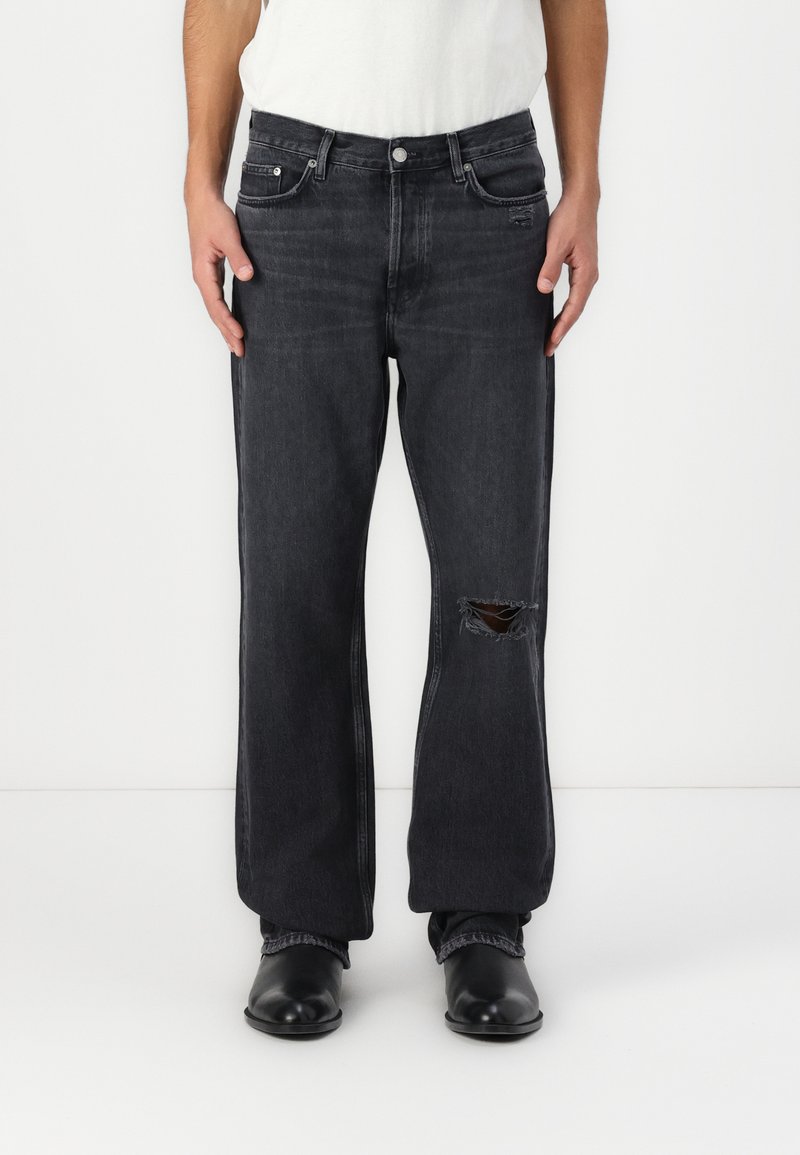 Black denim jeans with a relaxed fit, featuring a front pocket, a large cut-out on the left knee, and slightly frayed edges.