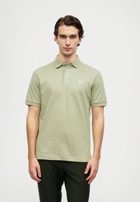 T-shirt polo em verde claro, feito de algodão, com colarinho, placket de três botões e um pequeno logótipo bordado no peito.