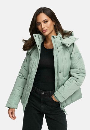 Lichtgroene pufferjack met een hoge kraag, ritssluiting en drukknoopsluiting, en een gestructureerd oppervlak. Gecombineerd met een zwarte top en donkere jeans.