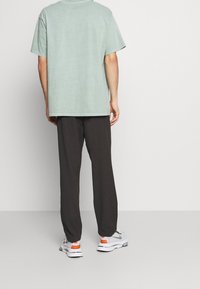 T-shirt mint pastel à manches courtes, ample, associé à un pantalon gris foncé. Détails notables : encolure ronde et design décontracté.
