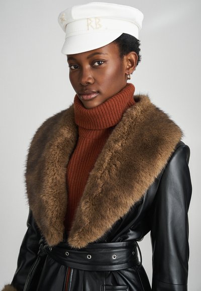 Melnas ādas mētelis ar brūnu kažokādas apkakli, kombinēts ar oranžu ribotu augstu apkakli un baltu cepuri ar zelta akcentiem.