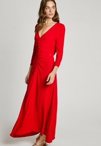 Robe maxi rouge à manches longues avec un décolleté en V profond et des détails de fronces sur le devant. Tissu doux et silhouette fluide.