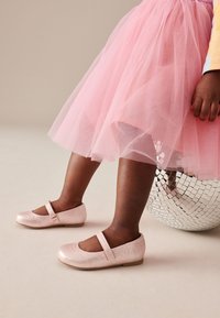 Rosa glitzernde Mary-Jane-Schuhe mit runder Kappe und einem einzelnen Riemen. Kombiniert mit einem fluffigen rosa Tüllrock, neben einer Diskokugel stehend.