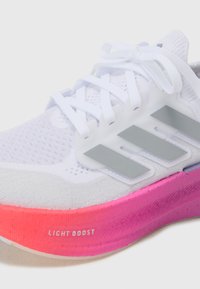 Vit atletisk sko med nätmaterial, tre grå ränder och en rosa gradient sula märkt "LIGHT BOOST." Har platta skosnören och vadderad krage.