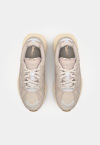 Beige atletiska skor med en texturerad mocka- och slät läderövre, med vita snören och en gummisula. Logotyp präglad på tungan.