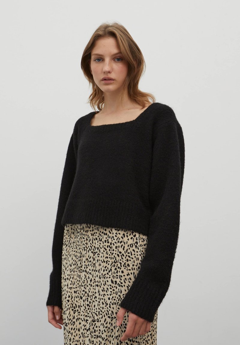 Zwarte cropped trui met een vierkante halslijn en lange mouwen, gemaakt van een gestructureerde stof. Draagt over een beige rok met luipaardprint.