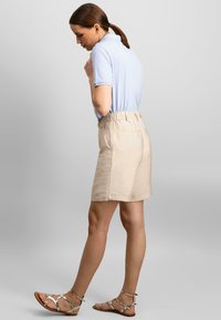 Lyseblå polo t-shirt stoppet ned i beige shorts med elastisk talje. Sandalerne har flere stropper og en flad sål.