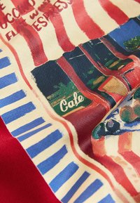 Tkanina z motivom kavarne, z rdečimi in belimi črtami skupaj z modrimi in belimi črtami. Besedilo "Cafe" je napisano z zelenimi črkami na temnem ozadju.