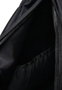 Vue intérieure d'un sac en tissu noir ouvert montrant une ouverture zippée et une poche intérieure cousue.