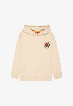 Beżowa bluza z kapturem z przednią kieszenią i pomarańczowym detalem graficznym. Połączona z luźnymi szarymi dżinsami i czarnymi trampkami z białymi podeszwami.