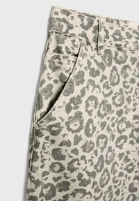 Tissu beige avec motif léopard gris sur pantalon montrant une poche, une passants de ceinture et des coutures détaillées.