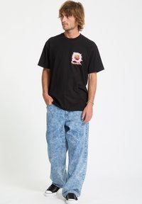 Camiseta negra con un diseño gráfico en el lado izquierdo del pecho; combinada con jeans de pierna ancha en azul claro; zapatillas negras; ajuste casual.