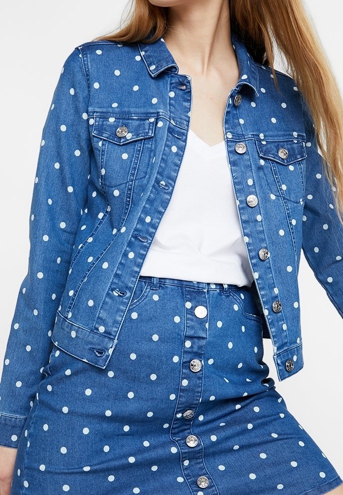 Denim jacket and matching button-up skirt with white polka dots worn over a white V-neck top.