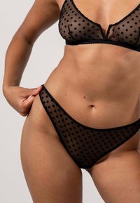 Zwart stippen lingeriesetje van doorschijnend gaas. Bevat een bralette met een V-hals en bijpassende low-rise slipjes met kantafwerking.