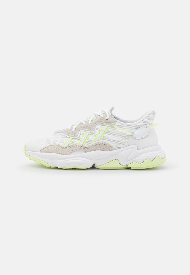 Zapatillas de malla blanca y ante, con acentos en verde neón, una suela gruesa con patrones en forma de ola y cordones.