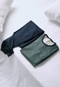 Dunkelblaues Langarmshirt und gemusterte grüne Schlafanzughose liegen auf einer weißen Fläche, aus weichem Stoff mit elastischen Bündchen.