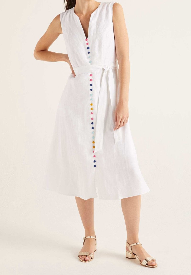 Robe midi blanche sans manches avec des boutons multicolores sur le devant et une ceinture nouée à la taille, portée avec des talons blocs ouverts dorés.
