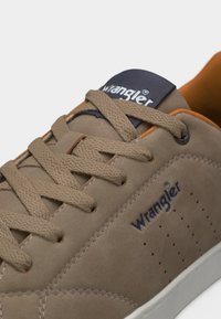 Ταν δερμάτινο παπούτσι Wrangler με υφή στα κορδόνια, διάτρητη πλευρική επιφάνεια, σήμα στη γλώσσα και πλευρά, λευκή σόλα και πορτοκαλί εσωτερική επένδυση.