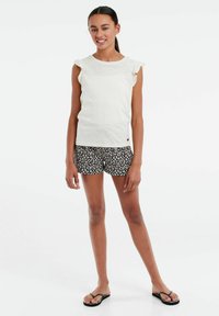 Hvid kortærmet top med detaljer i form af flæser på skuldrene, parret med shorts i sort blomsterprint. Model iført sorte flip-flops. Enkel, afslappet stil.