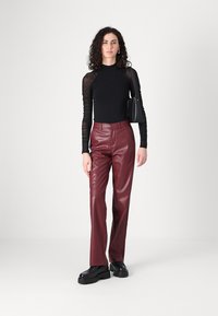 Haut noir à manches longues avec des manches rayées en tulle, pantalon en simili cuir bordeaux et chaussures noires à semelles épaisses. Un simple sac à main noir accentue le look.