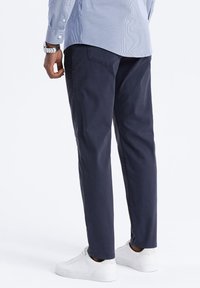 Pantalons en coton bleu marine avec une coupe droite et des ourlets à revers, associés à des baskets blanches. La chemise est bleu clair avec des rayures verticales.