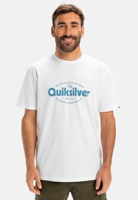 Bílý bavlněný tričko s modrým grafickým logem, na kterém je napsáno "Quiksilver" a další text. Krátké rukávy a design s kulatým výstřihem.