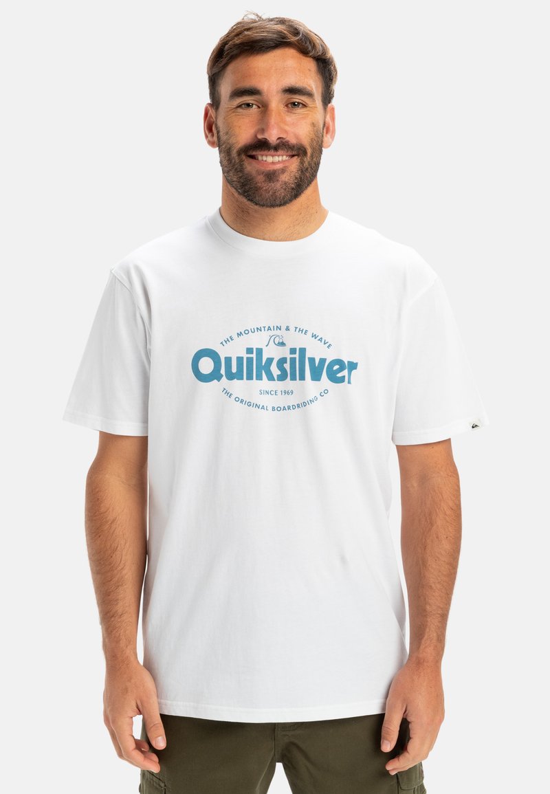 Camiseta de algodón blanca con un logotipo gráfico azul que dice "Quiksilver" y texto adicional. Diseño de mangas cortas y cuello redondo.