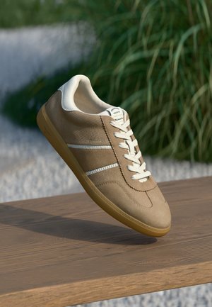 Brown suede sneaker with white accents, flat laces, and textured upper. Lightweight design and gum rubber sole. Classic athletic style.