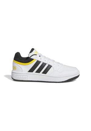 Zapatilla blanca de Adidas con rayas negras, detalles amarillos en el talón y la lengüeta, forro interior negro y suela blanca con suela exterior negra.