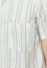 Camisa de lino blanca de manga corta con rayas verticales en azul claro, que presenta un frente abotonado y un bolsillo de parche en el lado izquierdo.