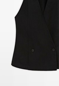 Černá na míru šitá vesta bez rukávů s hlubokým výstřihem do V a dvěma knoflíky u pasu na bílém pozadí.