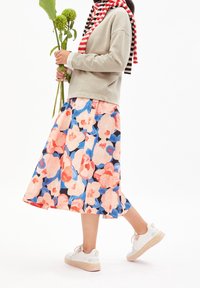 Květinová sukně má velké růžové a modré květy na tmavém podkladu, doplněná světle šedou mikinou a bílými teniskami s růžovými podrážkami.