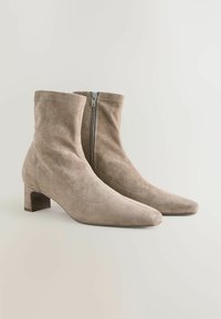 Beige suede ankle boots with a pointed toe and mid-height block heel; side zipper and seamless design for a sleek appearance.